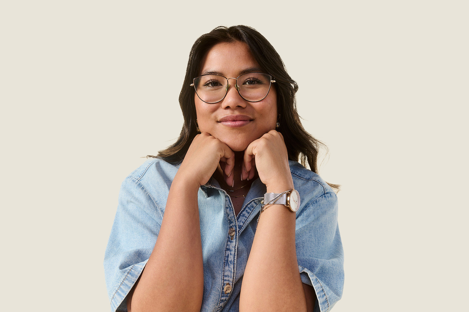 Junge Frau, asiatischen Ursprungs, mit Brille hat ihr Kinn auf ihre Hände gestützt und blickt lächelnd in die Kamera.