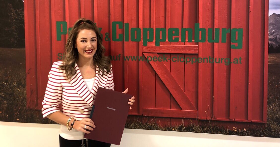 Unsere Abteilungsleiterin Antonella steht mit einer Bewerbungsmappe in der Hand vor einem roten Hintergrund mit P&C Logo.