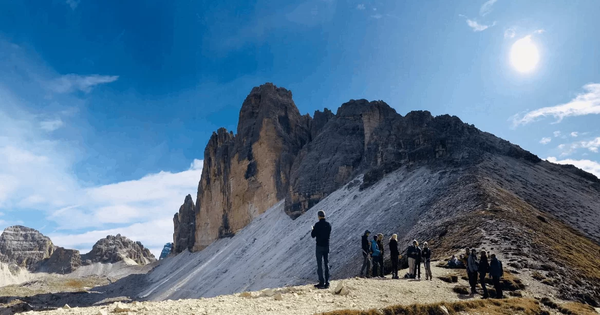 Menschen beim wandern auf einem Berg, im Hintergrund vereinzelte Wolken, blauer Himmel und strahlender Sonnenschein.